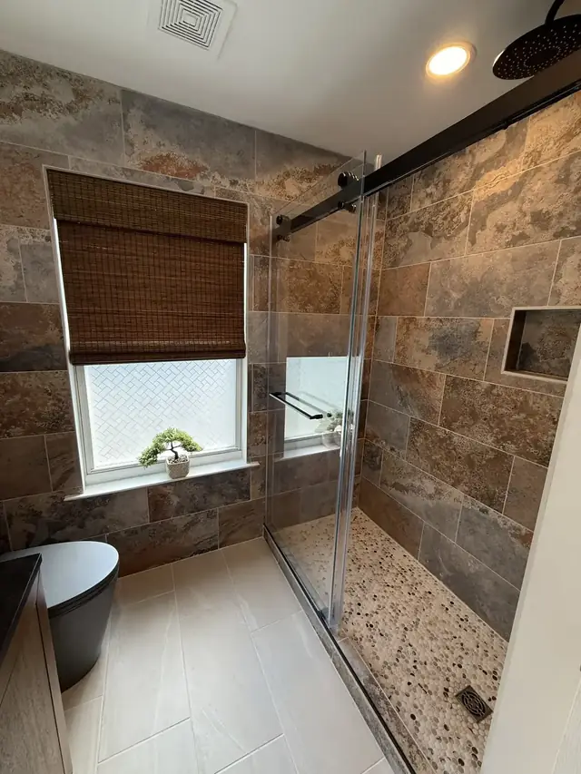 After: walk-in shower in slate-look porcelain with a pebble floor and matte black fixtures