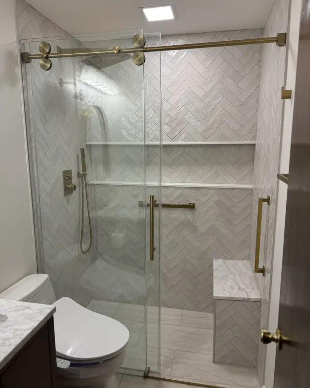 Glass shower with herringbone tile and brushed gold fixtures