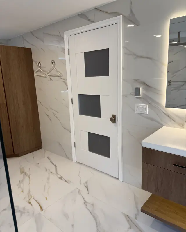 Marble-look bathroom with a wood linen cabinet and a backlit mirror