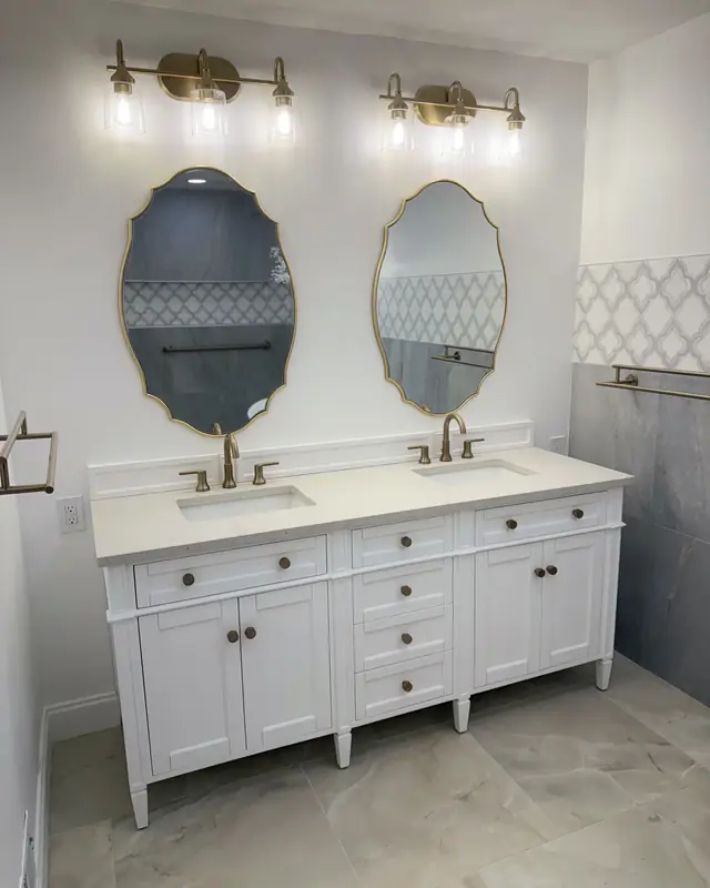 White double vanity with oval mirrors and a marble-look floor