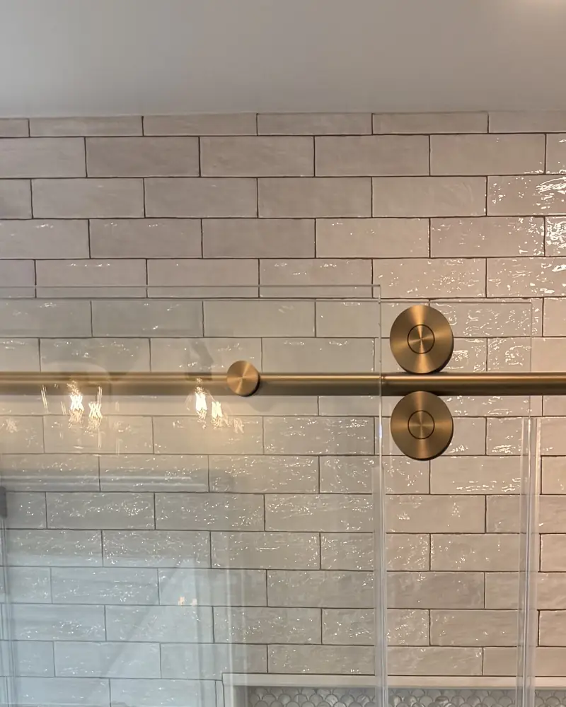 Brushed-gold rollers and bar on a frameless sliding shower door, against white subway tile