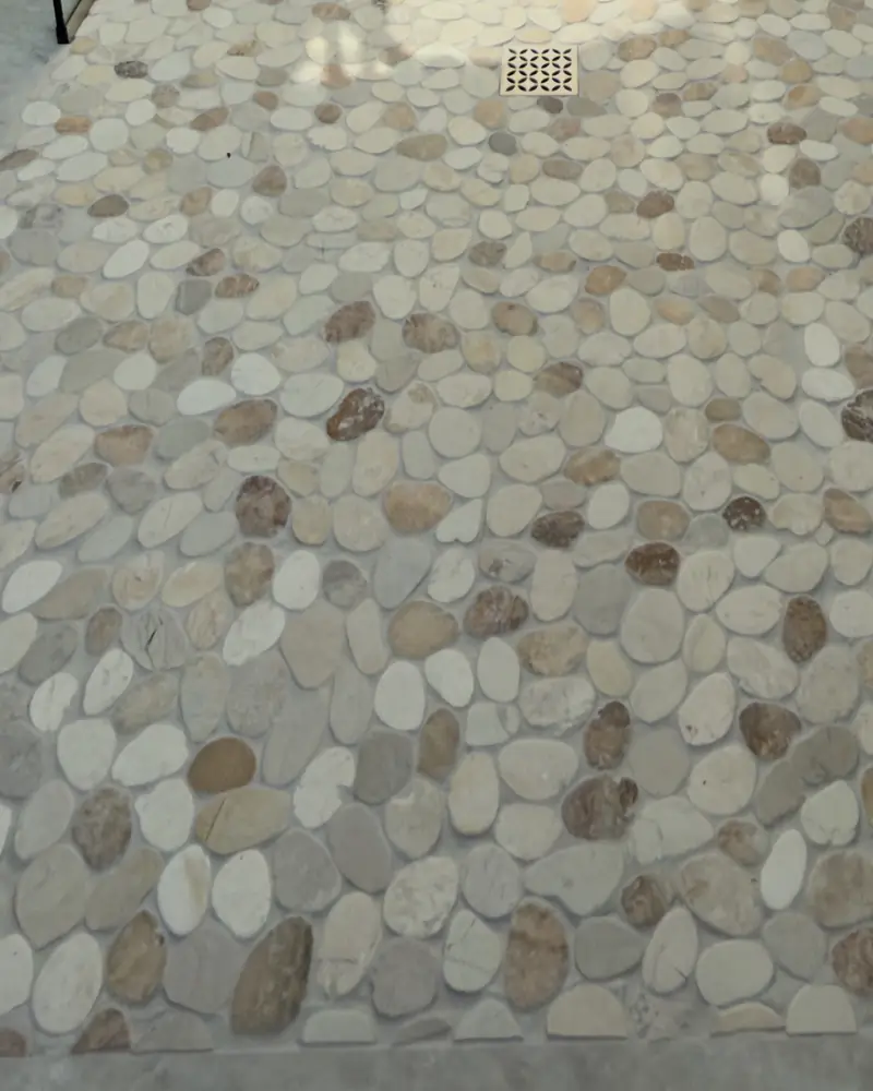 Close-up of a natural pebble shower floor meeting large-format porcelain with no curb