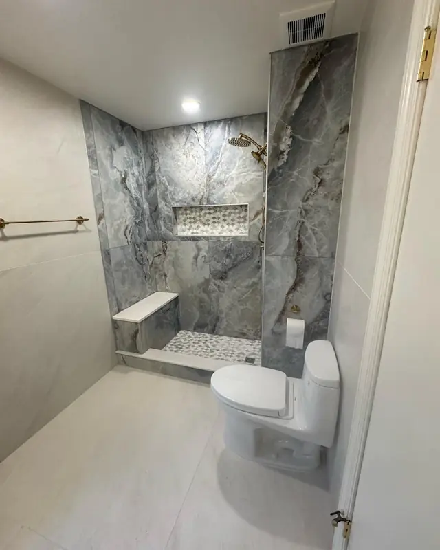 Walk-in shower with gray marble-look walls, a corner bench and a pebble floor