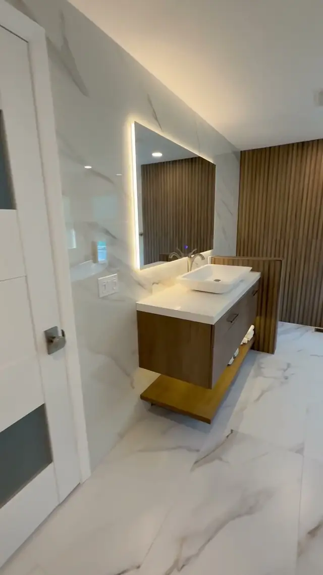 Primary bathroom in Burlington County, NJ: a floating walnut-look vanity with a vessel sink under a backlit mirror, beside a fluted wood wall