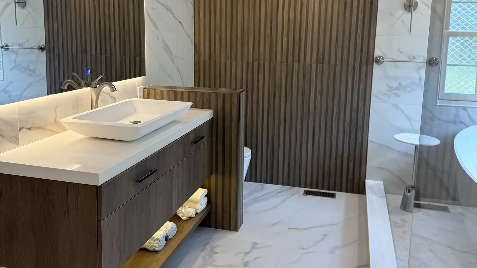 Primary bathroom with a walnut-look floating vanity, vessel sink, LED mirror and a fluted wood wall