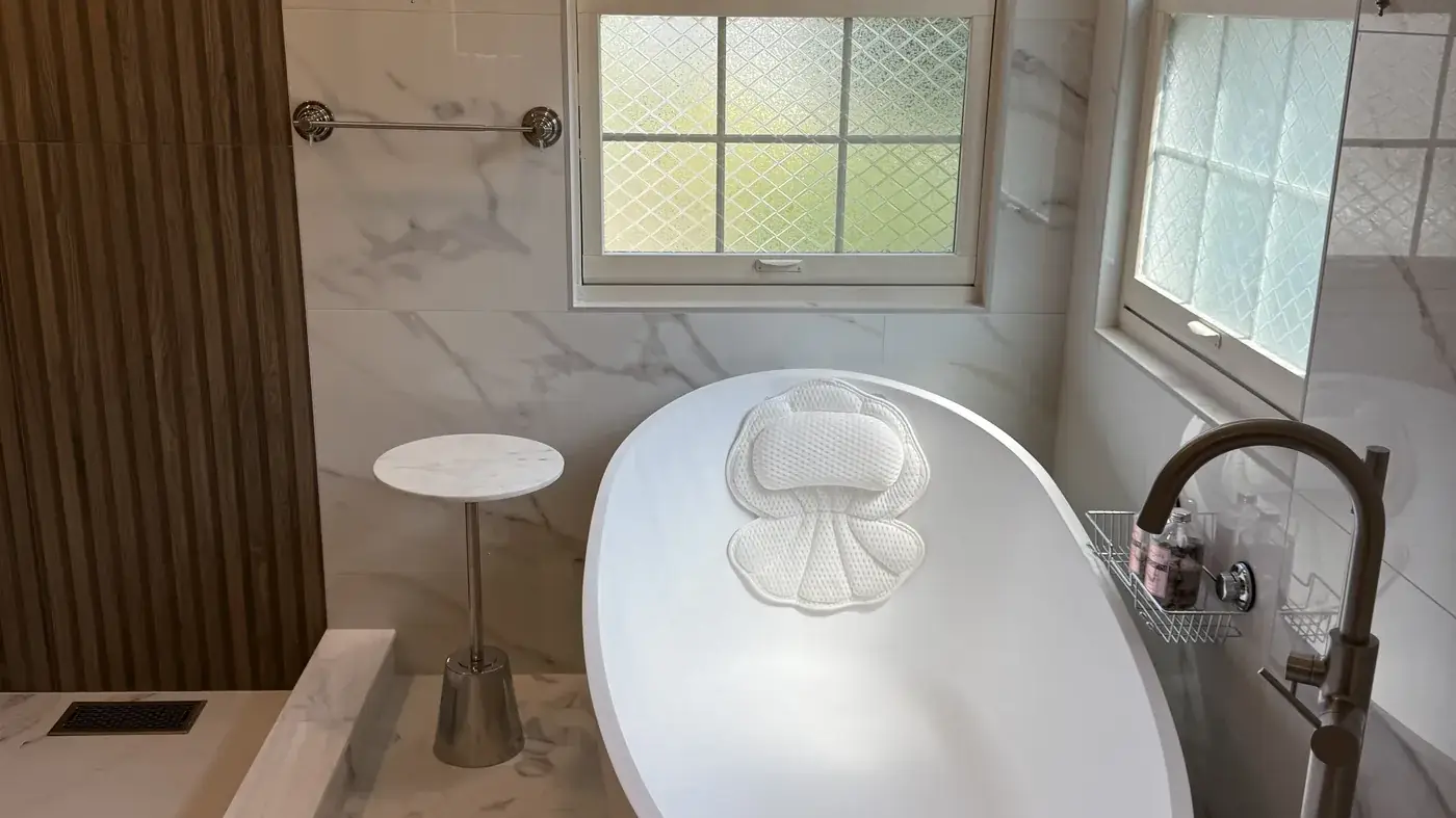 Freestanding tub by two windows in a primary bath with a fluted wood wall