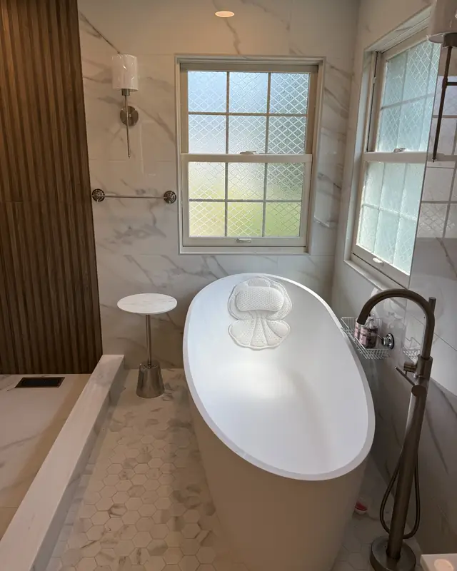 Freestanding tub next to a fluted wood wall and frosted windows