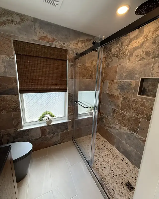 Tub-to-shower conversion in slate-look porcelain with a pebble floor and matte black sliding glass door