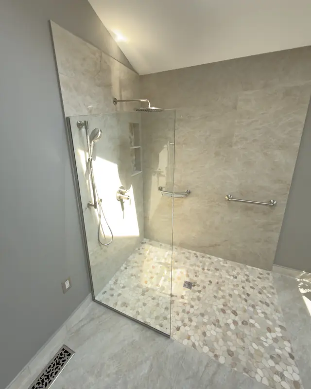 Curbless walk-in shower with a fixed glass panel, pebble floor and grab bars