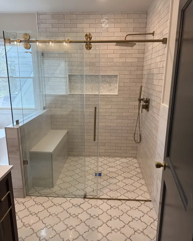 Walk-in shower with a brushed gold sliding glass door, built-in bench and white arabesque tile floor