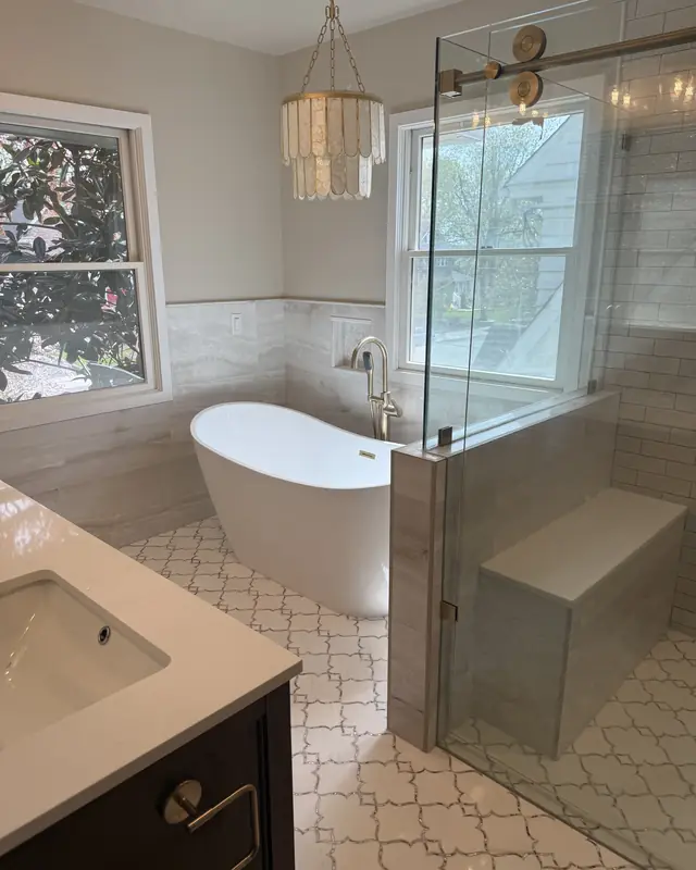 Freestanding tub by the window under a shell chandelier, next to a glass shower