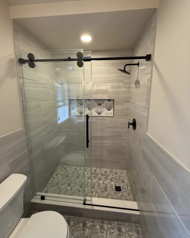 Guest shower with a matte black sliding glass door, patterned niche and patterned floor